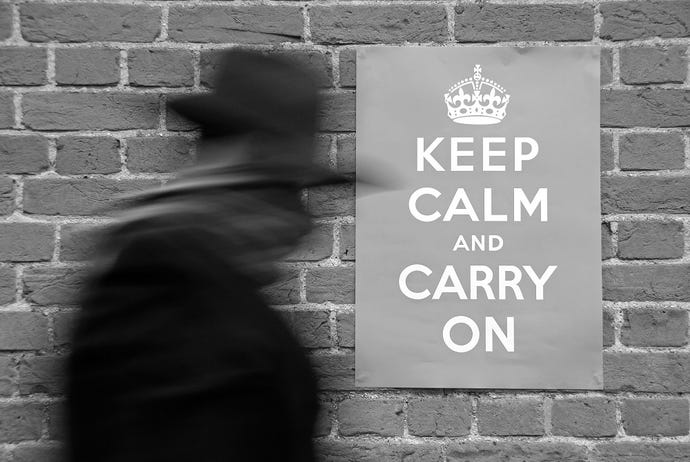 silhouette of person in hat walking past sign on wall reading "Keep Calm and Carry On"