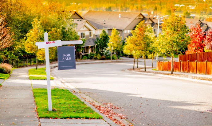 Photo of a For Sale sign on a tree-lined suburban street of single-family homes in autumn