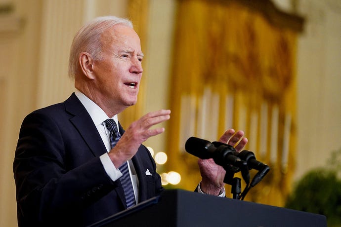 US President Joe Biden speaks at a lectern about Russia and Ukraine from the White House; he gestures above a bank of mics