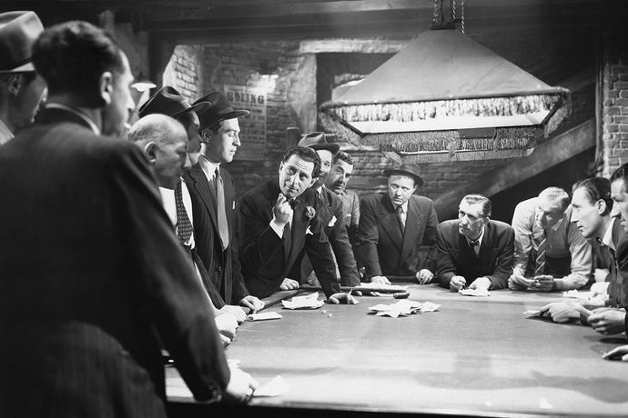Black-and-white photo of a group of mobsters having a meeting around a pool table