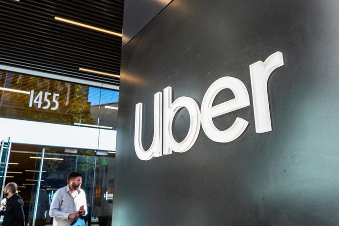 Photo contains image of Uber logo in corporate setting with man in the background