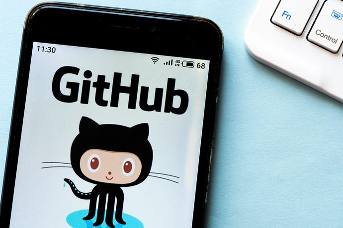 Photo of the GitHub kitty octopus logo thing on the screen of a smartphone lying on a desk next to a computer keyboard