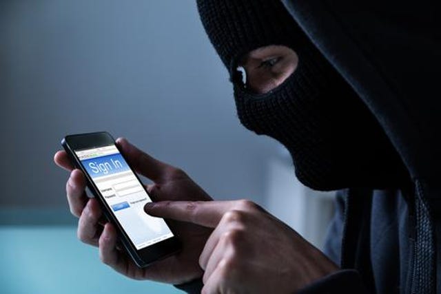 A person with a black mask over the face holding a phone receiver.