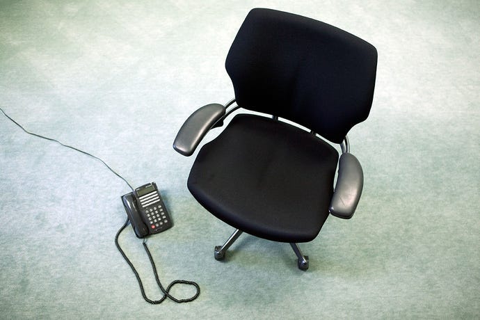 Photo of a basic black office chair and an office telephone sitting in an otherwise empty room