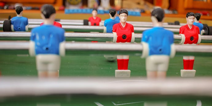 Photo of the figures on a foosball table, where you see the red team's faces and the blue team players are blurry