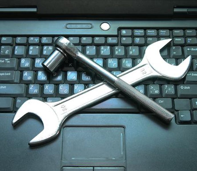 An open-end wrench and a socket wrench making an x on a laptop keyboard.