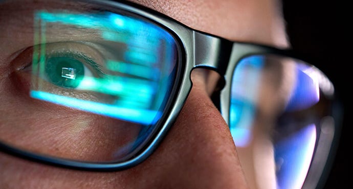 Analyst looking on computer, programming code reflecting in glasses.