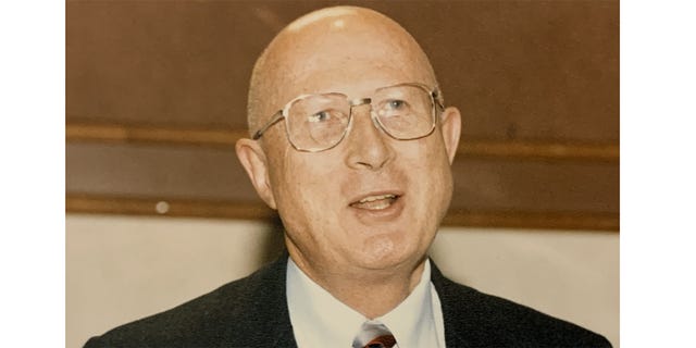 Donn B. Parker in a suit and tie, with metal-framed glasses and a conspicuously bald head