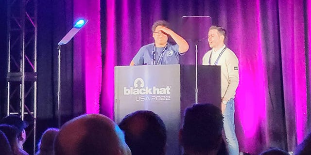 Martin Schwartzl, in a t-shirt and glasses, and Pietro Borrello, in a button-down shirt, at BHUSA 2022 podium