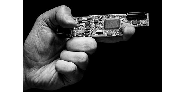 Black-and-white photo of a man's hand holding a circuit board to mimic a gun