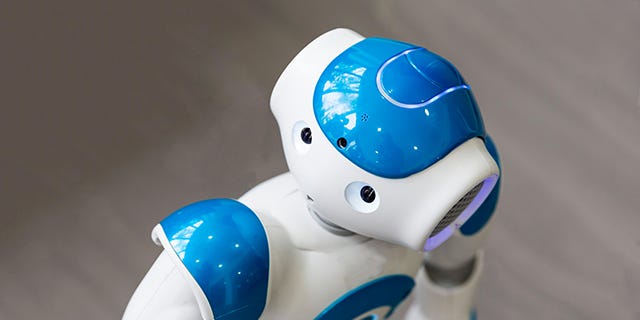 A small robot with humanoid face and body side-eyes the camera