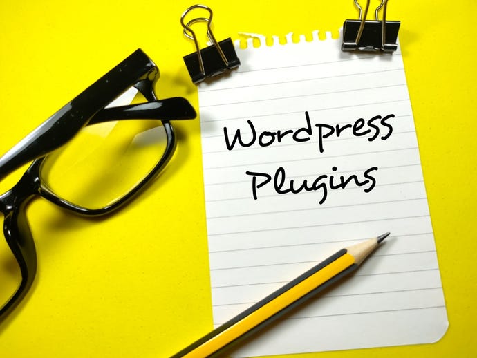 Wordpress plug-in writing on notepaper with pencil, paper clips and glasses on yellow background.