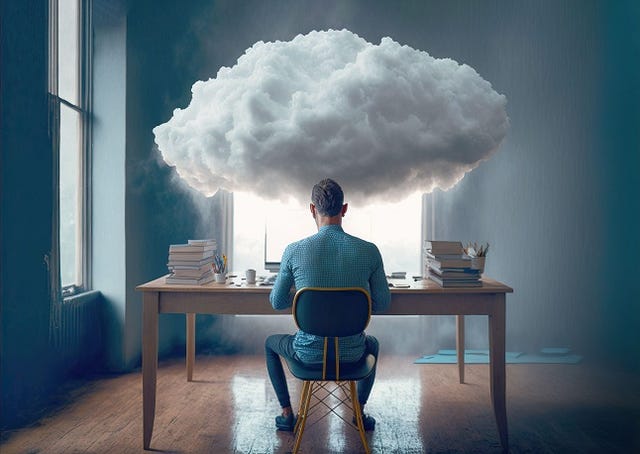 A person sitting at a desk with a computer with a cloud over his head, symbolizing the integration of cloud computing 