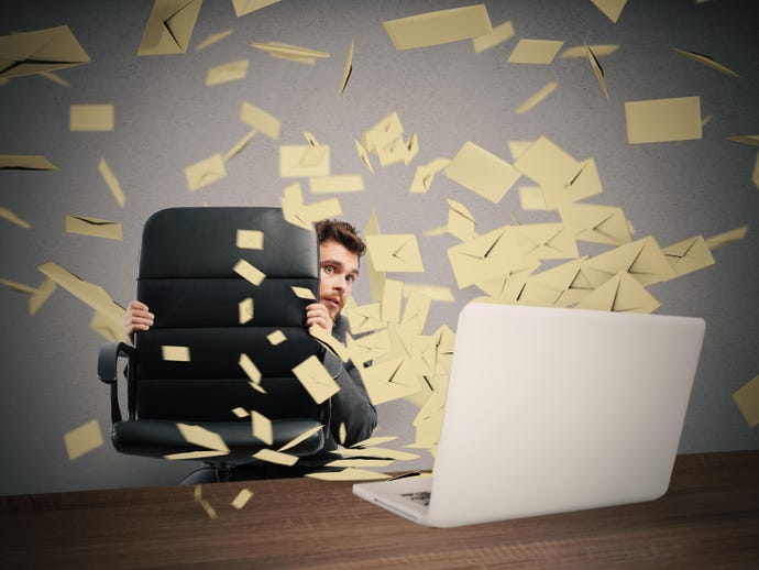Image shows frightened-looking man crouching behind a desk chair in front of a computer on a table while envelopes fly around
