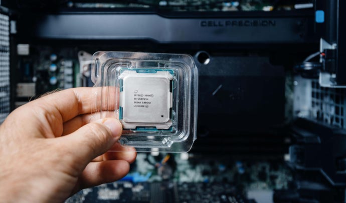 Male hand holding Intel Xeon E5-2687w v4 CPU processor in plastic blister pack with workstation innards in background