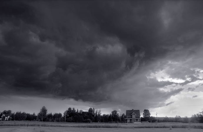A large black cloud over a house and a field