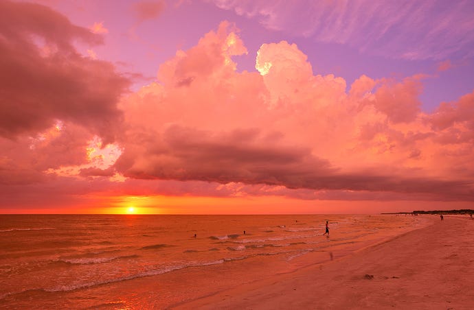 The sun sets into the white-capped waves of Gulf of Mexico near St. Pete, Florida; puffy clouds are orange and red