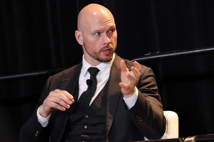 man in dark suit and tie speaks on a stage