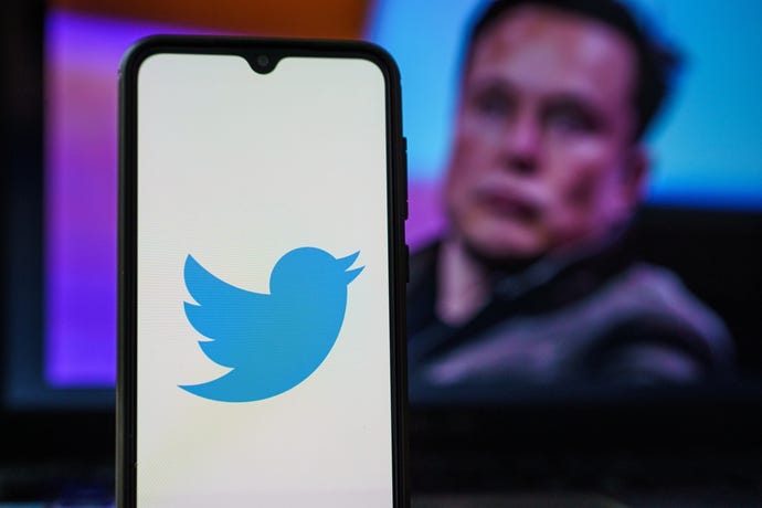 Twitter logo on smartphone and Elon Musk in the background. Elon Musk joins Twitter board