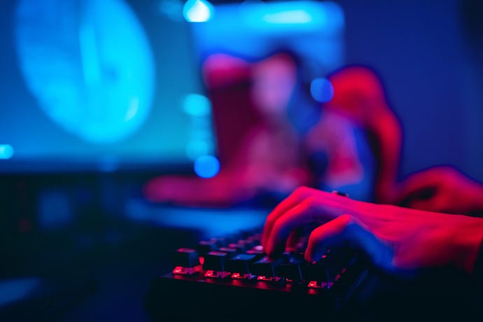 Image shows hands typing at keyboard lit by a red light with blurred human figures in the background