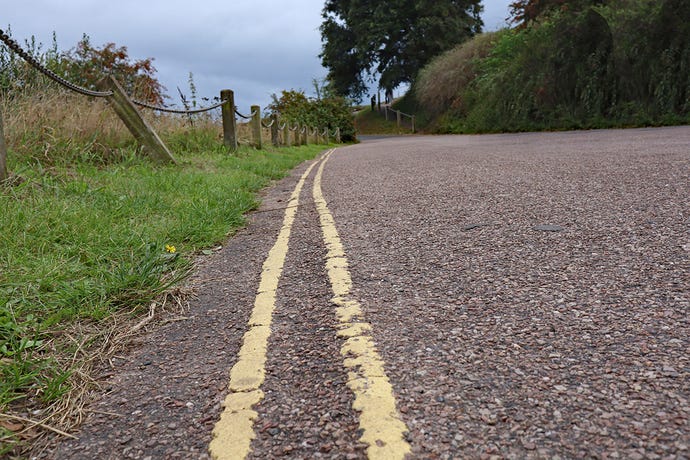 Low level closeup photo of double yellow lines on a narrow country lane, meaning no parking is allowed
