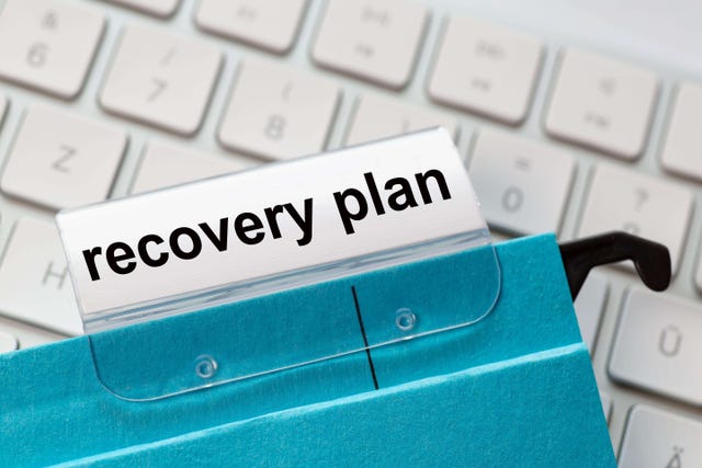 recovery plan is on a label of a blue hanging file. In the background a computer keyboard