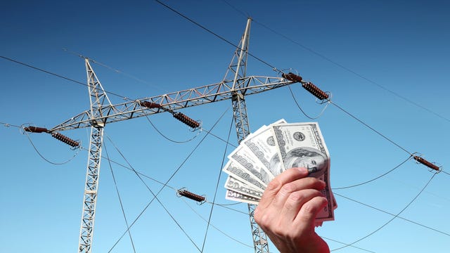 Concept image showing hand holding money in front of photo of power transmission lines