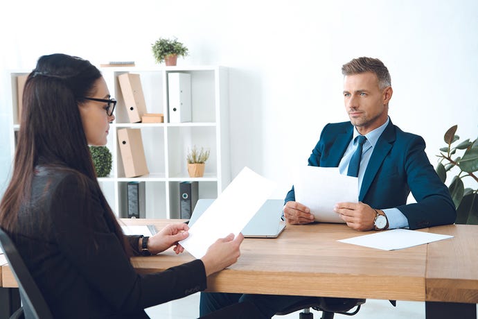 Two businesspeople, an Asian woman and a white man, go over paperwork at a desk