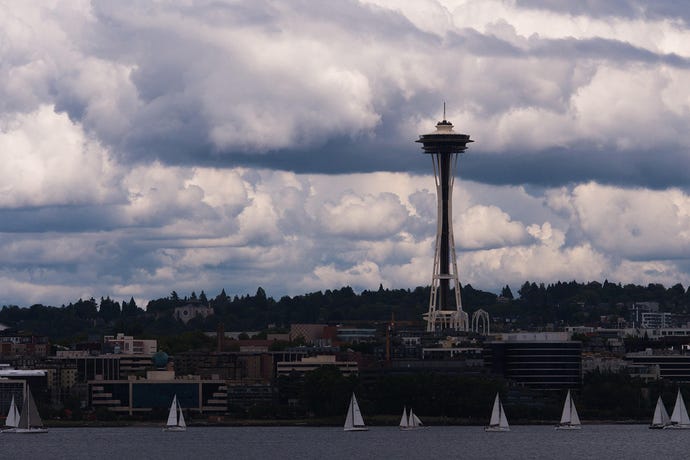 Seattle Space Needle shot from ferry on overcast afternoon with large clouds and multiple white sailed boats