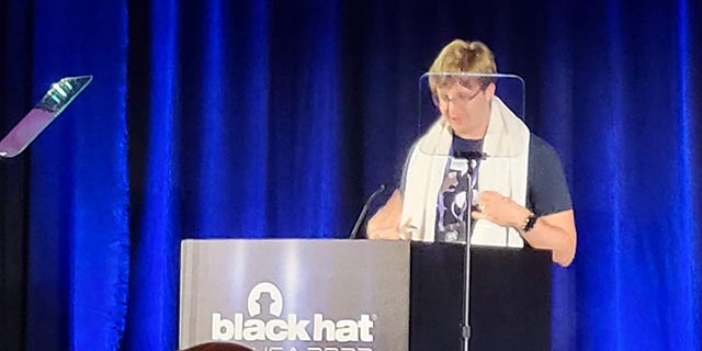 Hammond Pearce, a blond man wearing a graphic t-shirt with a towel draped over his shoulders, at a BHUSA 2022 podium