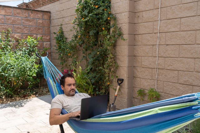 Bearded man relaxes in hammock with laptop in garden home office during covid quarantine