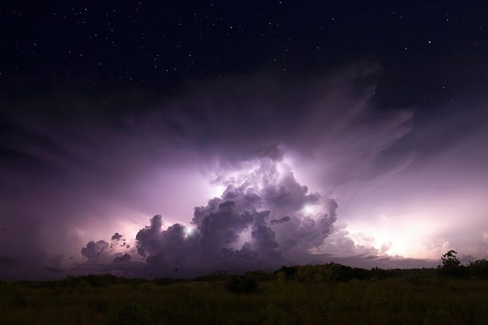 Image of a cloud burst on the horizon, with lightning lighting up a purple pile of clouds