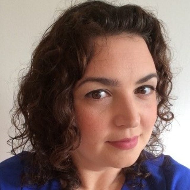 Curly-haired brunette woman wearing blue against a light background.