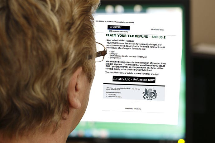 Photo from behind of a woman reading on a desktop computer a phishing email claiming she is entitled to a UK tax refund.