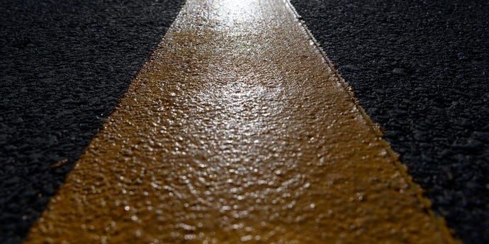 Abstract close-up of yellow line in the middle of a paved road.