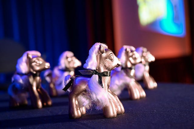 A closeup of six Pwnie awards, basically My Little Pony figurines spray-painted gold with black ribbons around their necks