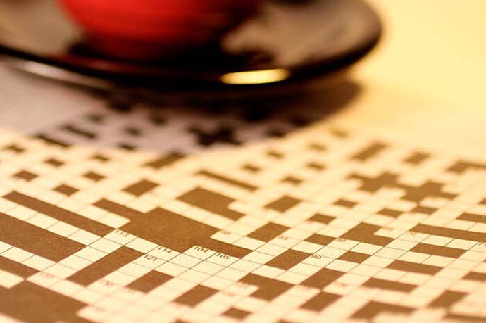 Crossword puzzle, cup and saucer on a table top.