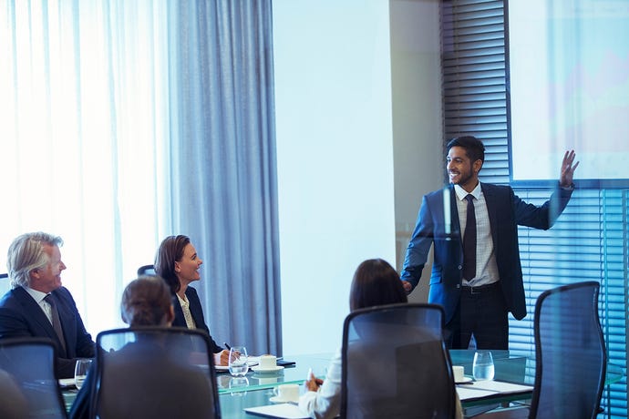 Photo of young bearded businessman giving formal presentation to older colleagues in conference room