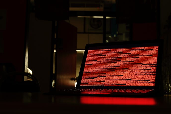 Ominous orange code on a laptop screen lights up a darkened room
