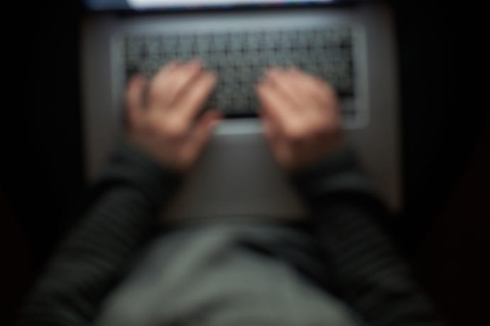 Blurry overhead shot of a hoodie-wearing hacker typing on a laptop