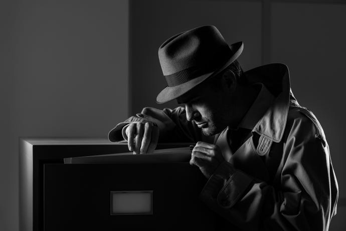man in old-fashioned spy outfit peering at a computer screen