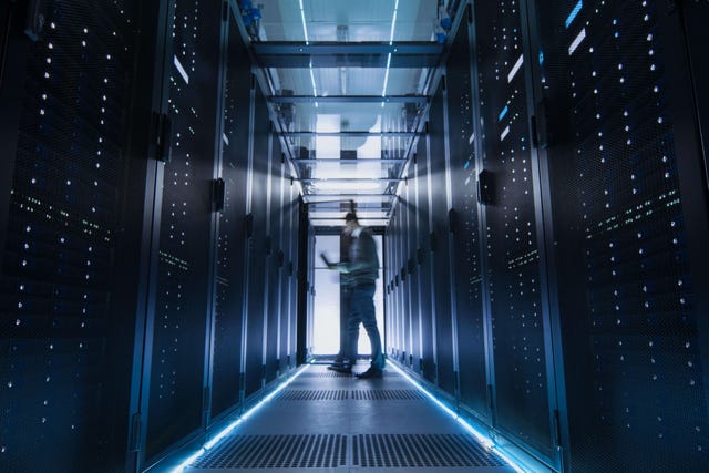 Male IT Engineer Walking and Working in Data Center Corridor. She is Holding Tablet Computer. He is Blurred in Motion