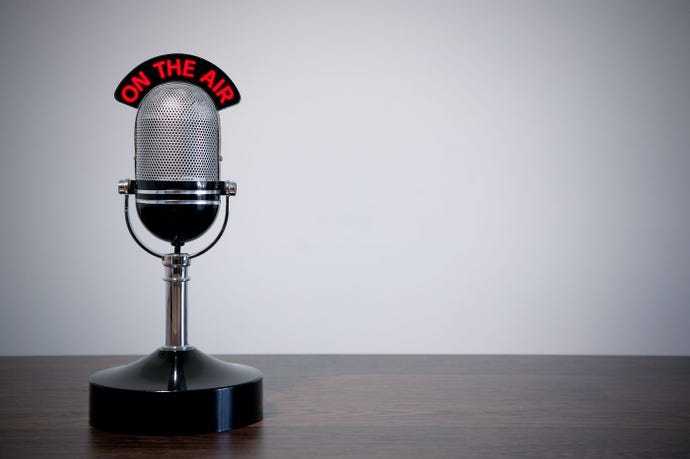 An old-fashioned upright microphone with an "on-air" sign on a desk against a neutral background.
