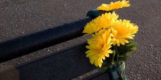 A bouquet of yellow flowers tied to the side of a park bench in a memorial.