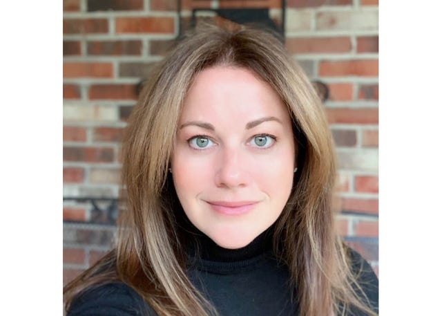 A woman standing in front of a brick wall while wearing a black turtleneck sweater.