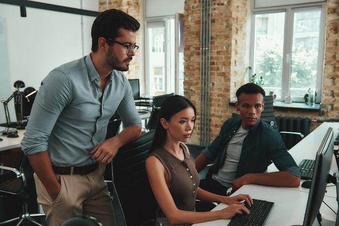 Multiethnic group of young IT employees looking at computer monitor and discussing something while sitting in modern open space.