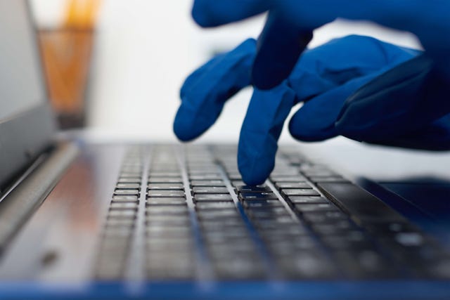 Photo of hands in blue protective gloves typing on a laptop keyboard. Cyber crime and protection concept