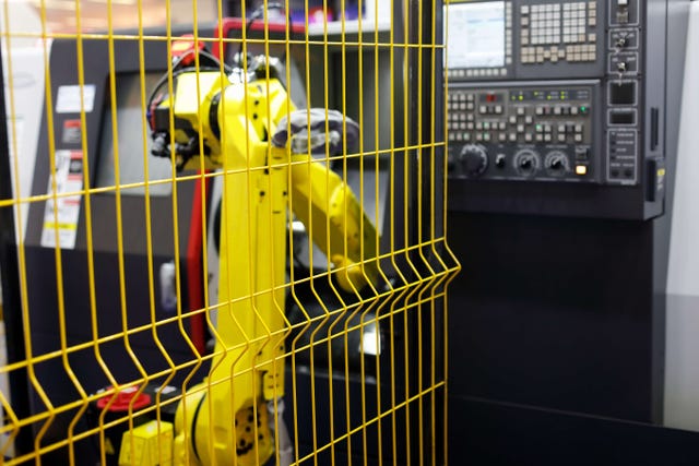 Photo of a yellow industrial robot arm behind a yellow safety cage