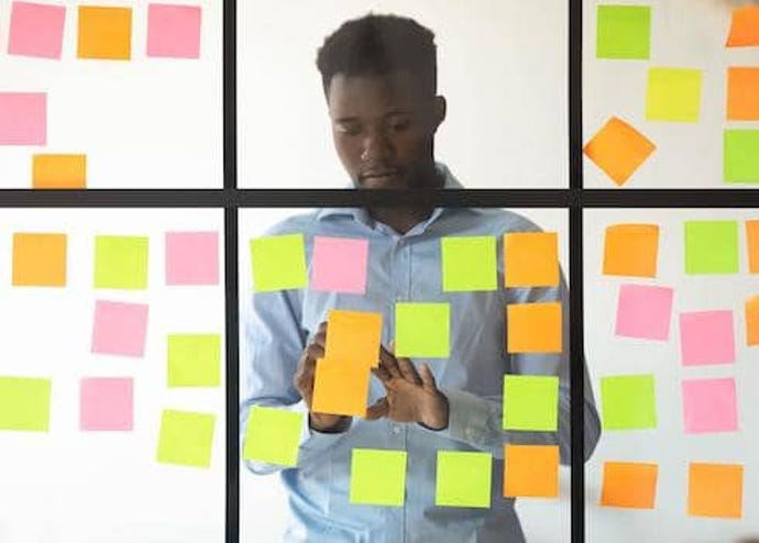 young man arranging Post-It notes on a window, representative of an app development board