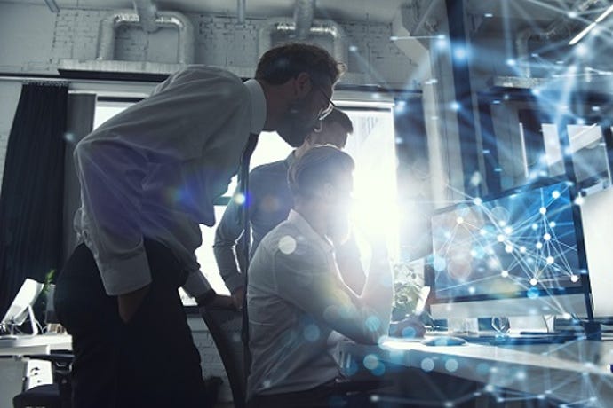 Two people leaning over and watching what the third person is doing on the computer.